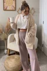 woman wearing a cozy cream oversized cardigan and a white cropped top, paired with blush wide-leg pants, holding a mug