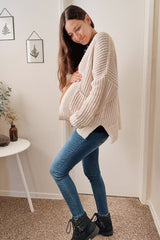 woman wearing a cream chunky knit cardigan and blue skinny jeans, holding her baby bump