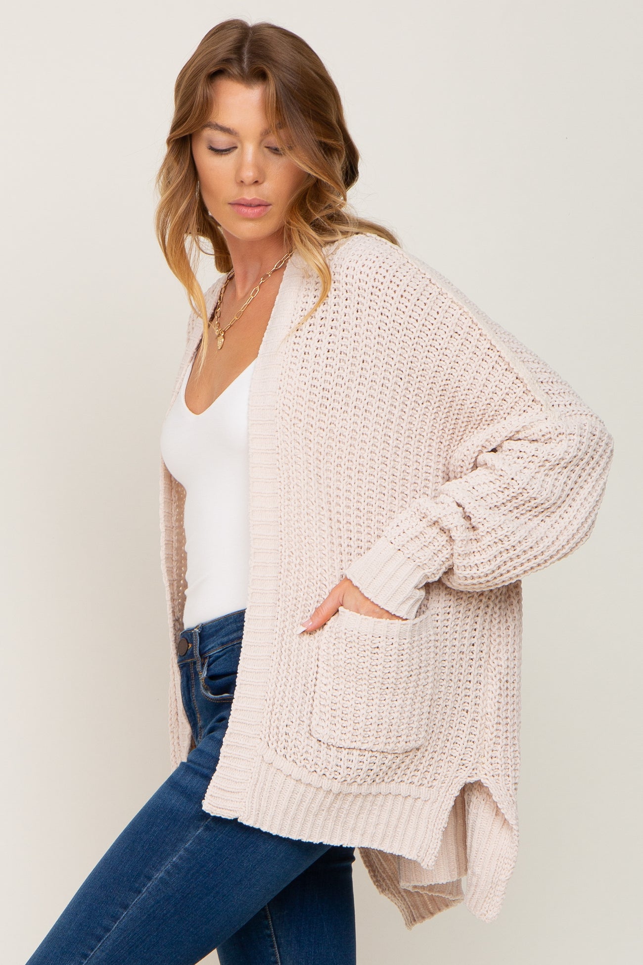 woman wearing a light pink knitted cardigan with side pockets, paired with a white top and blue jeans