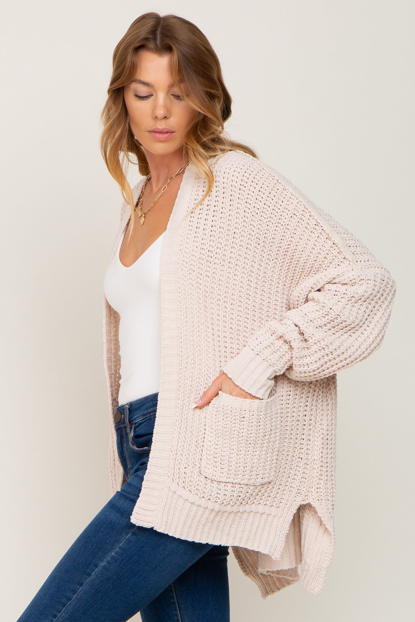 woman wearing a light pink knitted cardigan with side pockets, paired with a white top and blue jeans