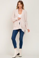 woman wearing a light pink open-knit cardigan with pockets over a white top and blue skinny jeans
