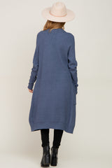 woman wearing a long blue maternity cardigan with a loose fit and side pockets, facing away from the camera