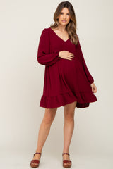 pregnant woman wearing a burgundy long sleeve maternity dress with ruffle hem and v-neckline