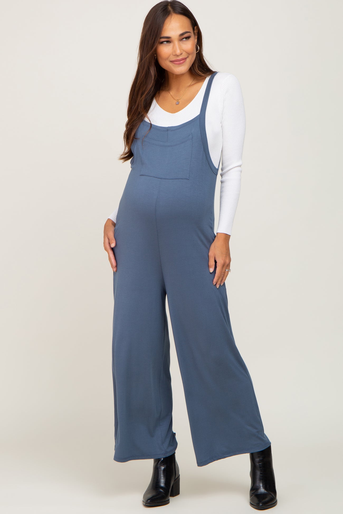 woman wearing a blue maternity jumpsuit with a white long sleeve top and a visible baby bump