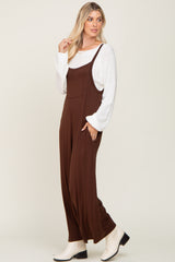 Woman wearing a brown wide-leg jumpsuit over a white long-sleeve sweater and cream ankle boots