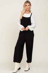 woman wearing a black jumpsuit over a white sweater and white ankle boots