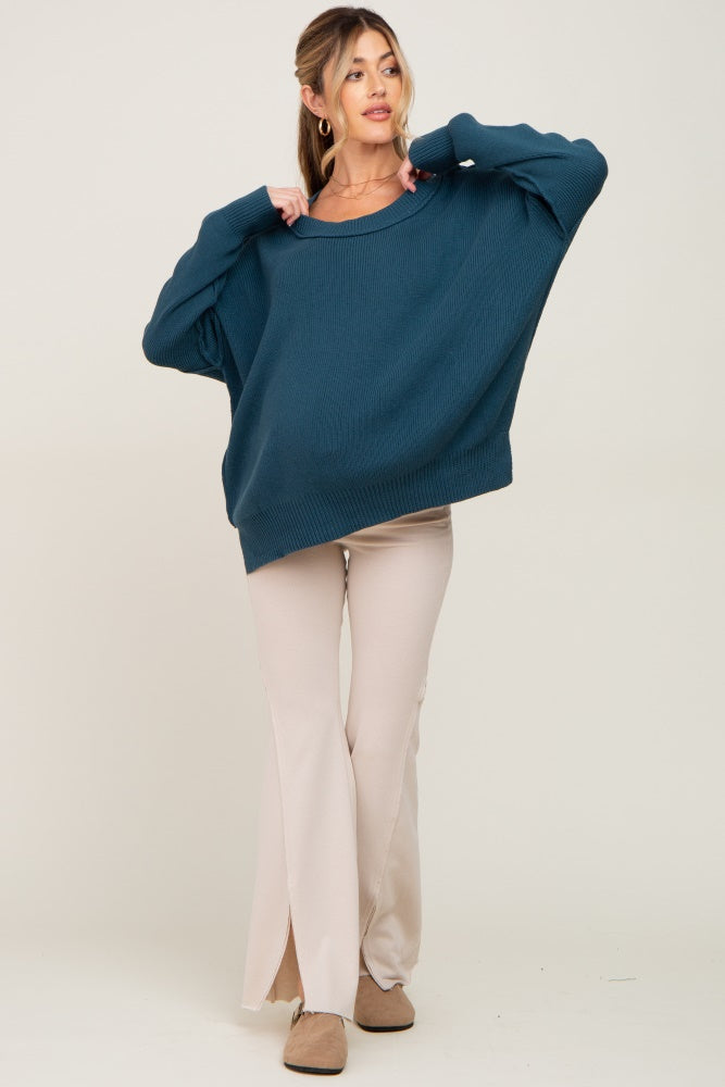 woman wearing a teal oversized knit maternity sweater and beige flared maternity pants