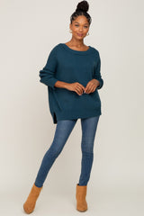 woman wearing a teal oversized knit sweater with side slits and blue skinny jeans, paired with tan ankle boots