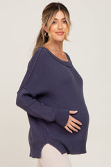 woman wearing a navy maternity sweater with a loose fit and side slits, gently cradling her baby bump