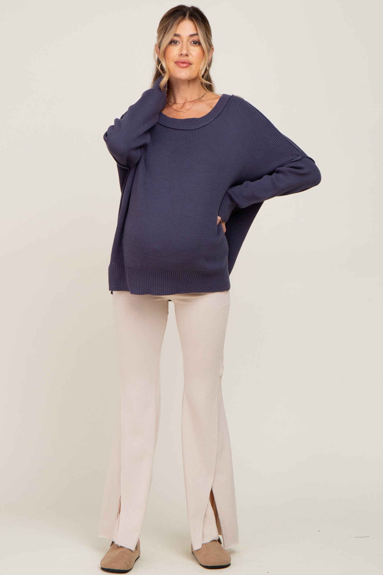 woman wearing a navy blue oversized maternity sweater and cream-colored flared pants, showing her baby bump
