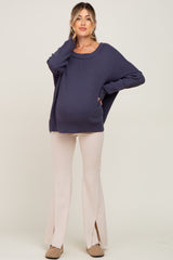 woman wearing a navy blue oversized maternity sweater and cream-colored flared pants, showing her baby bump