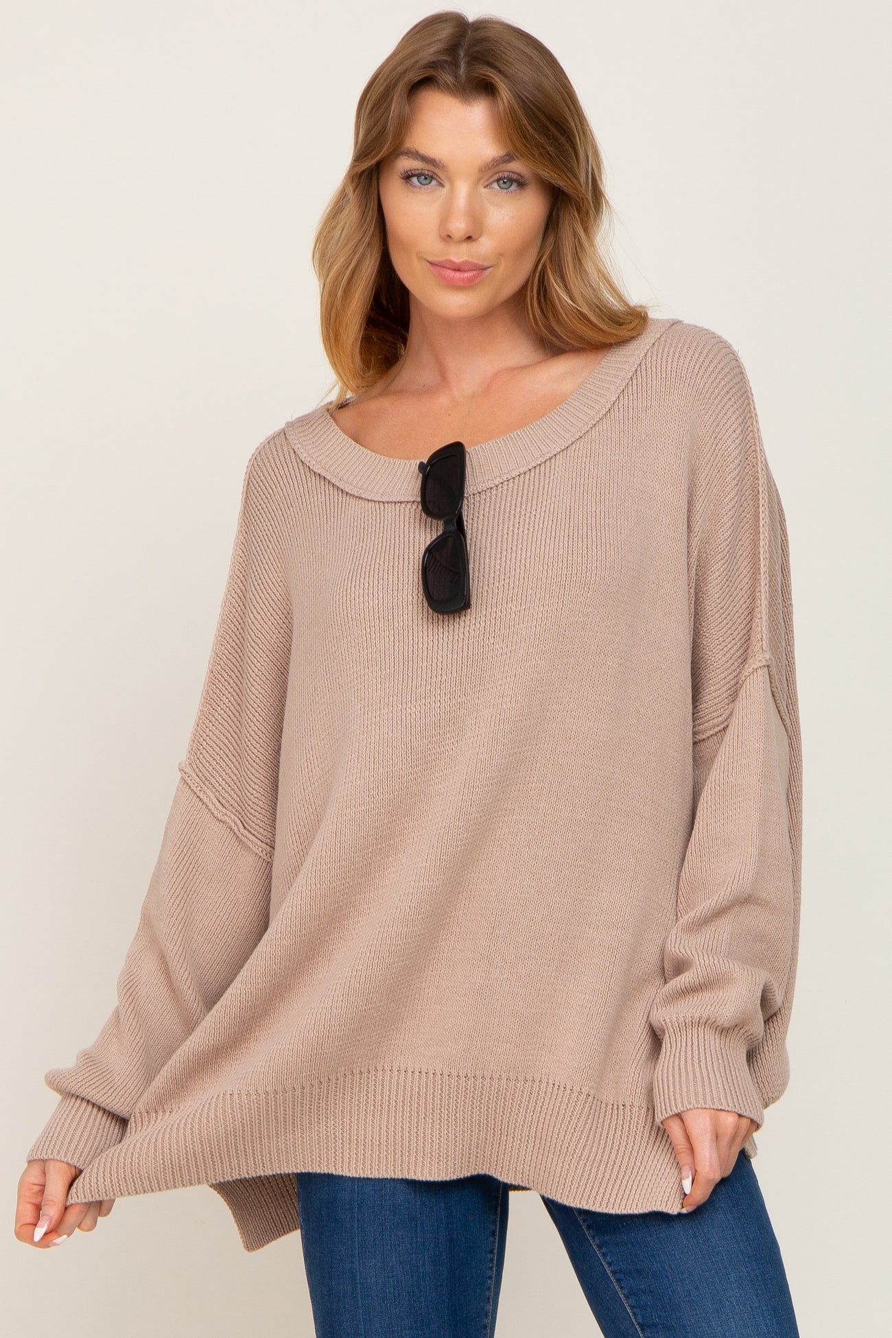 woman wearing a beige oversized sweater with a wide neckline and long sleeves, paired with blue jeans