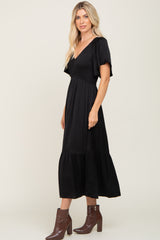 Woman wearing a black smocked midi dress with flutter sleeves and brown crocodile boots