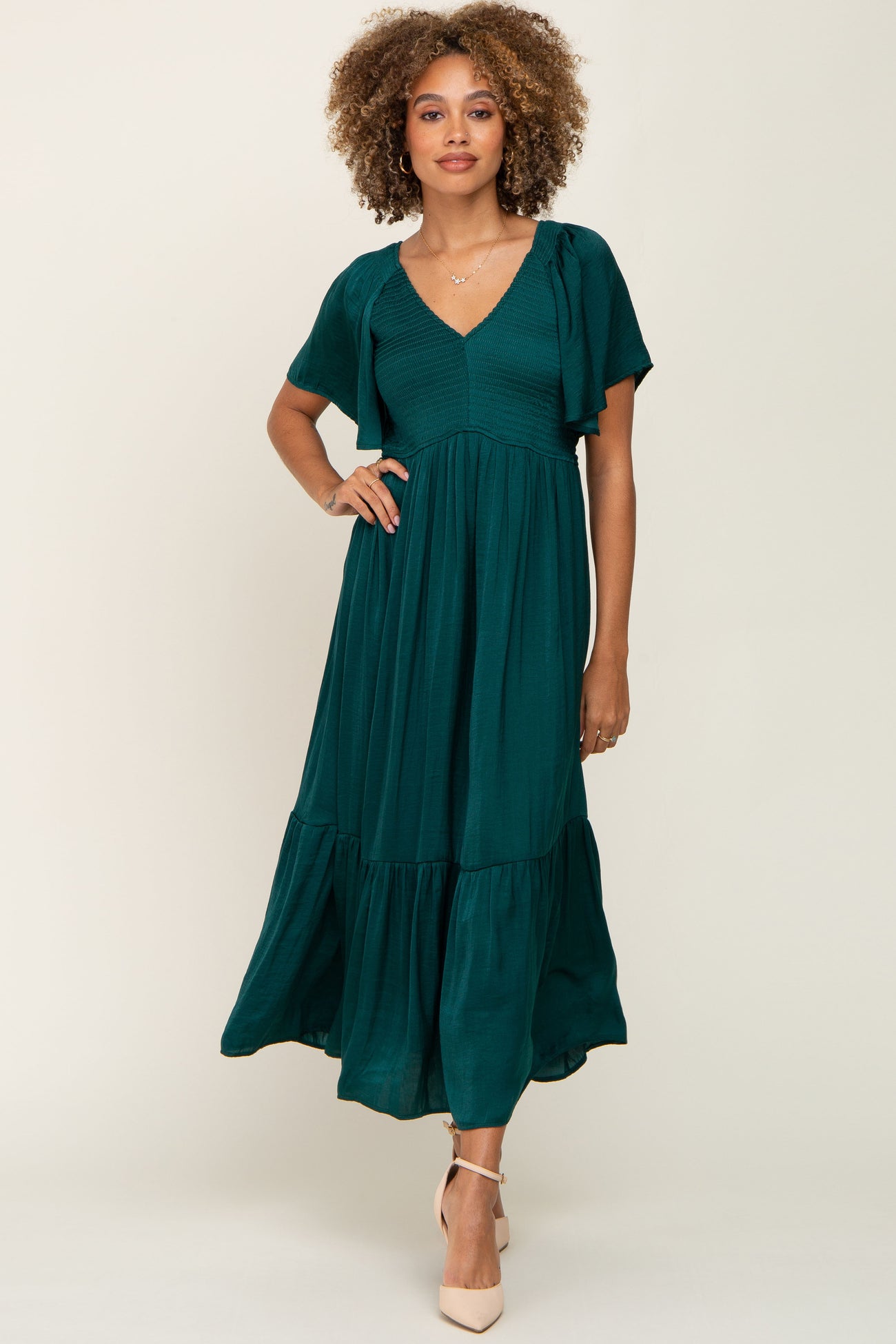 woman with curly hair wearing a dark emerald green v-neck midi dress with flutter sleeves and tiered skirt