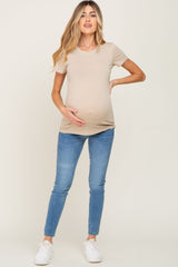 woman wearing a beige short sleeve maternity top and blue skinny jeans, holding her baby bump