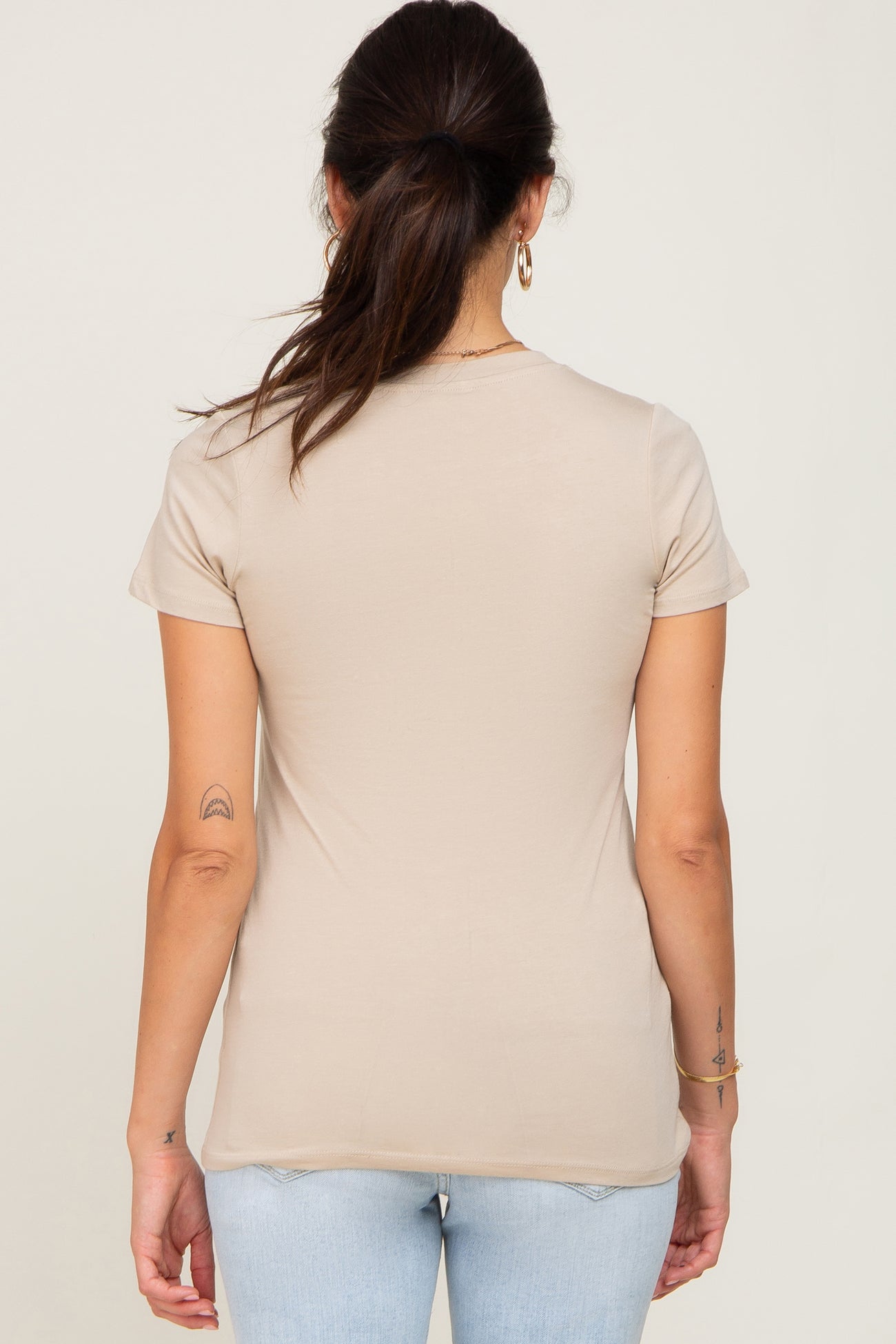woman wearing a beige short sleeve fitted t-shirt, seen from the back, paired with light blue jeans