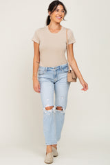 woman wearing a light beige fitted t-shirt and distressed light blue jeans, carrying a small handbag and wearing slip-on shoes