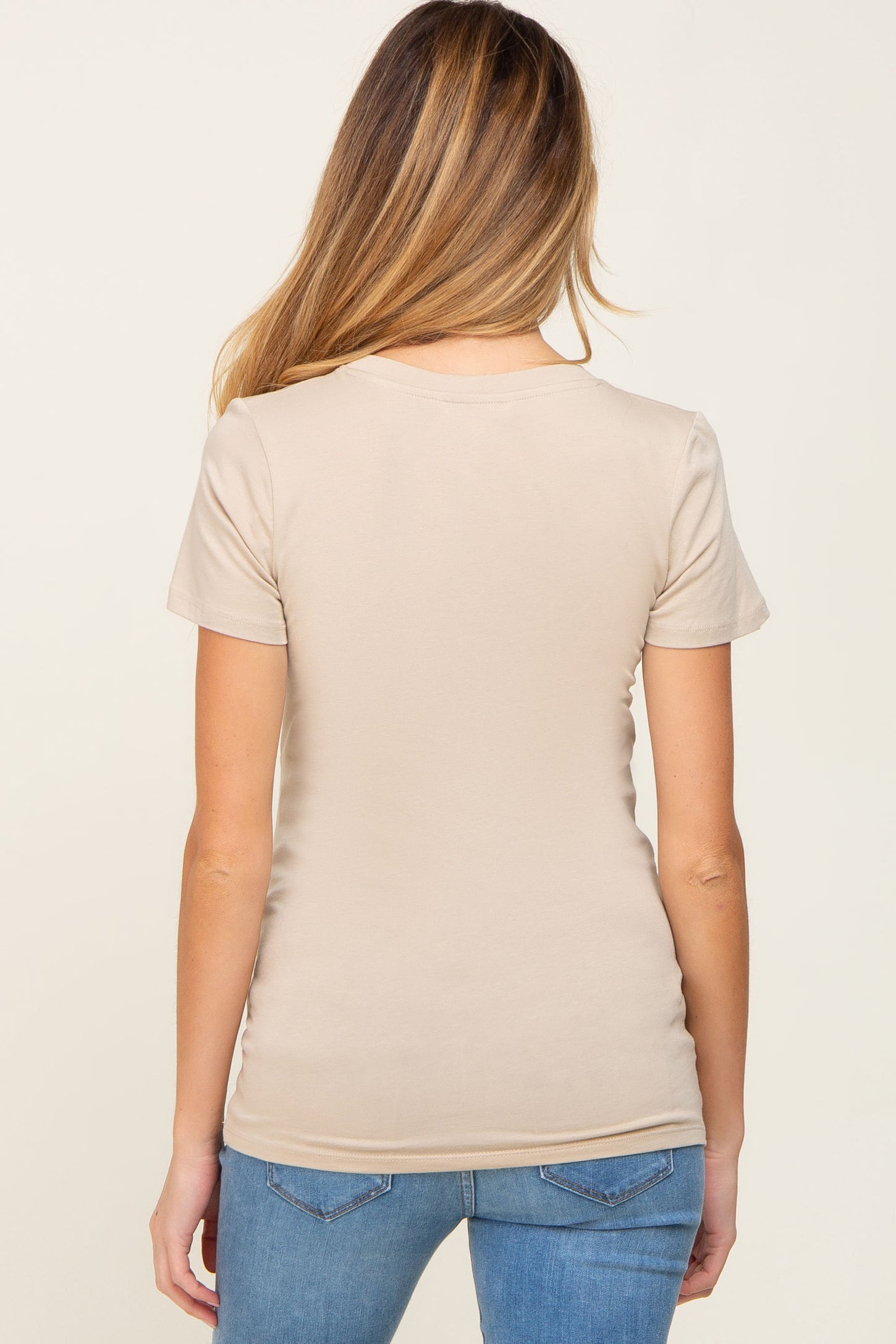 woman wearing a beige short sleeve maternity top, viewed from the back, paired with denim jeans