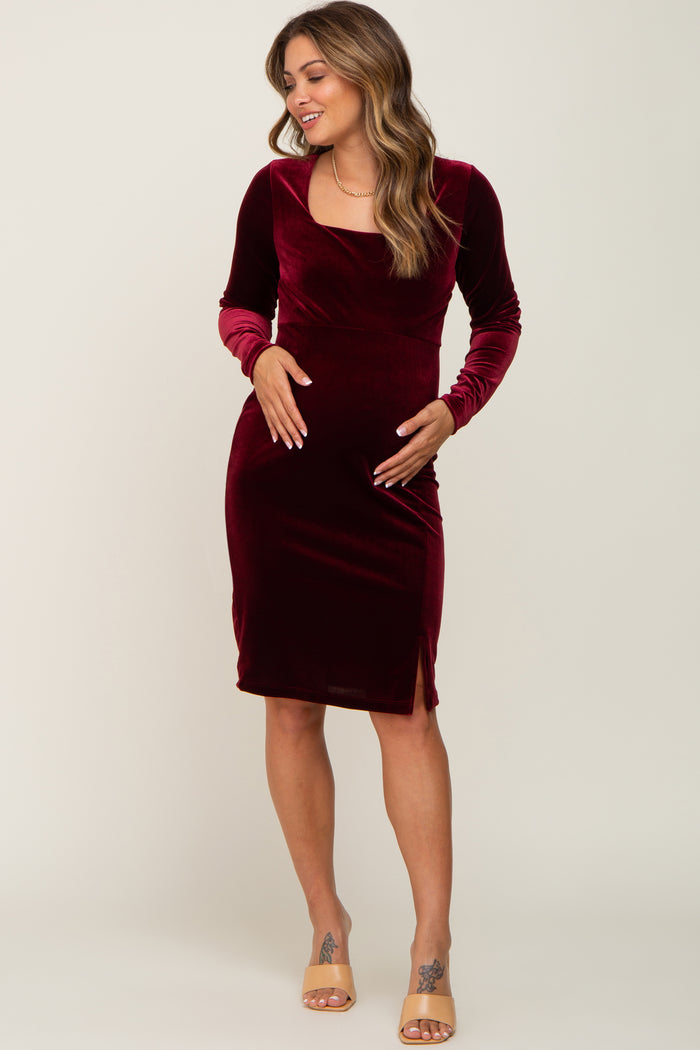 woman wearing a burgundy velvet maternity dress with long sleeves and a side slit, highlighting her baby bump