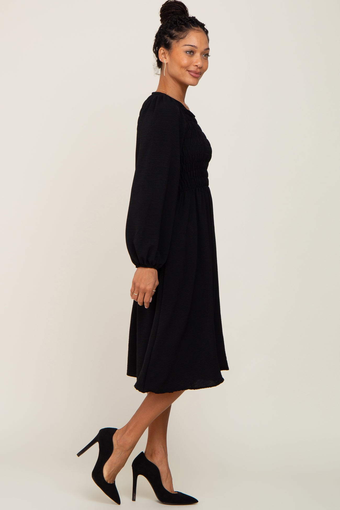 woman wearing a long sleeve black smocked midi dress and black high heel pumps