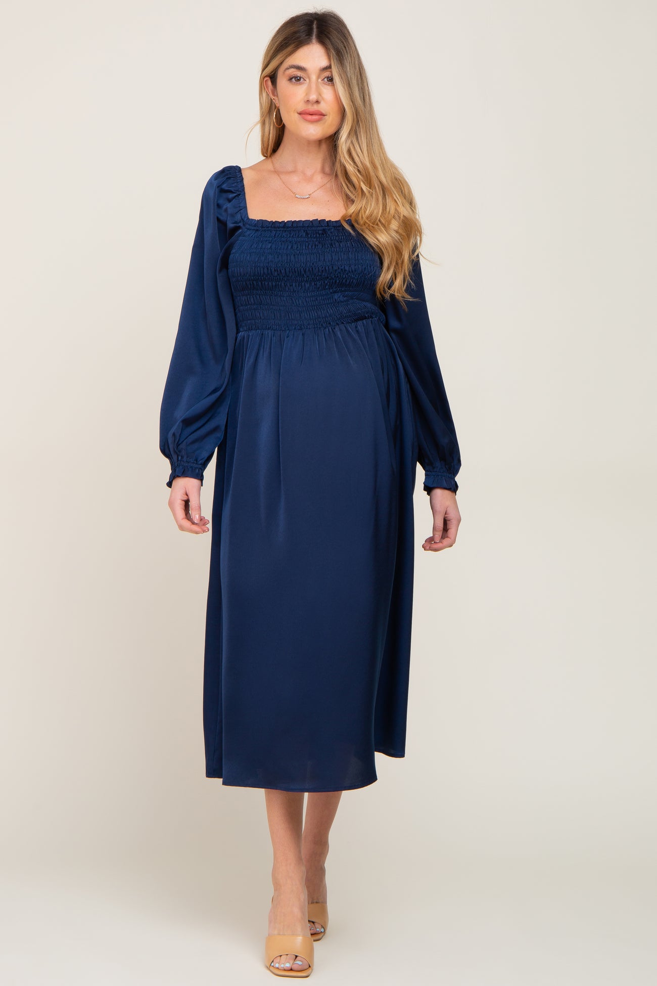 woman wearing a navy blue long sleeve maternity dress with a smocked bodice and a flowing skirt, baby bump visible