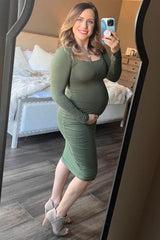 pregnant woman in olive green long sleeve maternity dress taking mirror selfie in bedroom