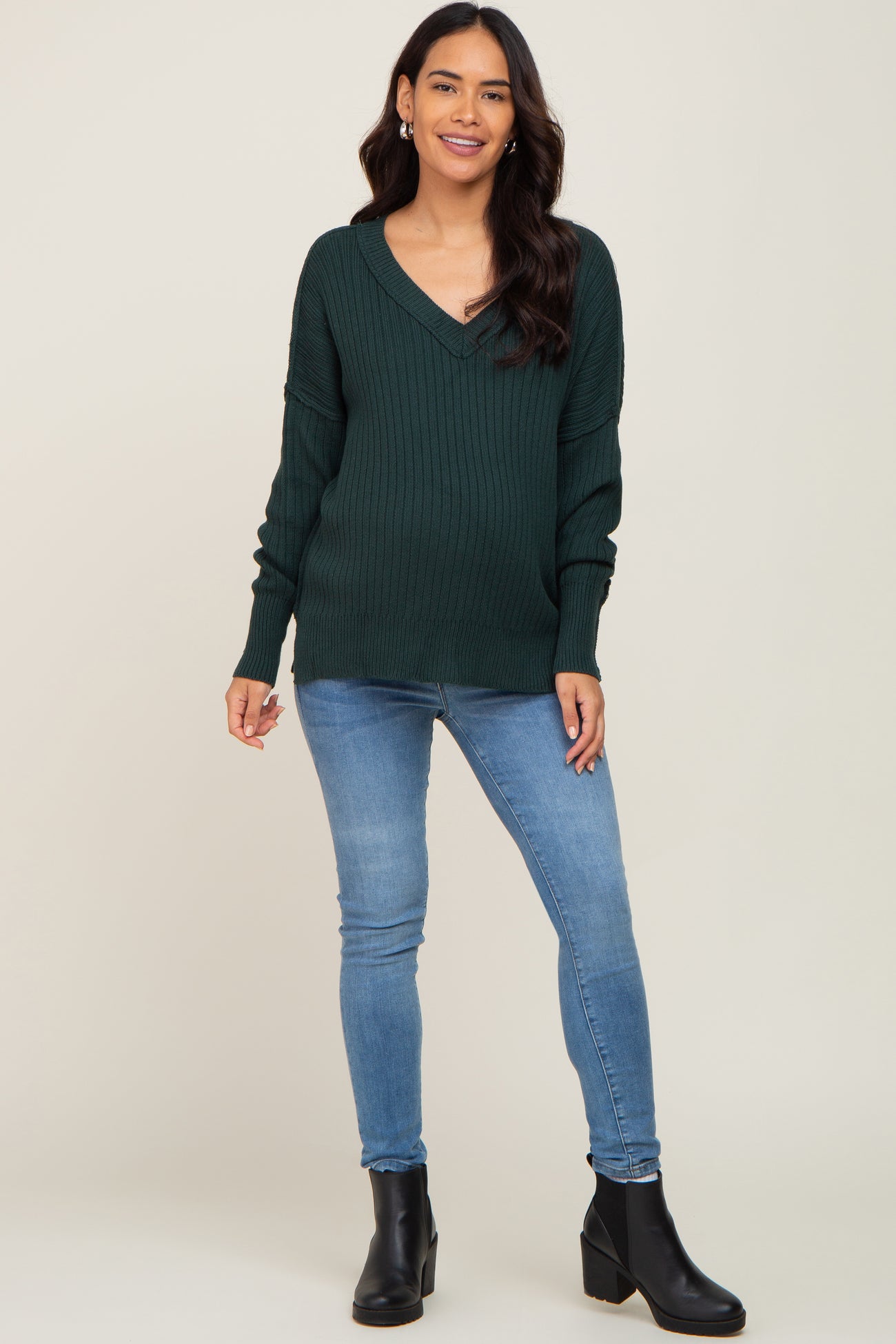 woman wearing a dark green v-neck ribbed maternity sweater with blue skinny jeans and black boots
