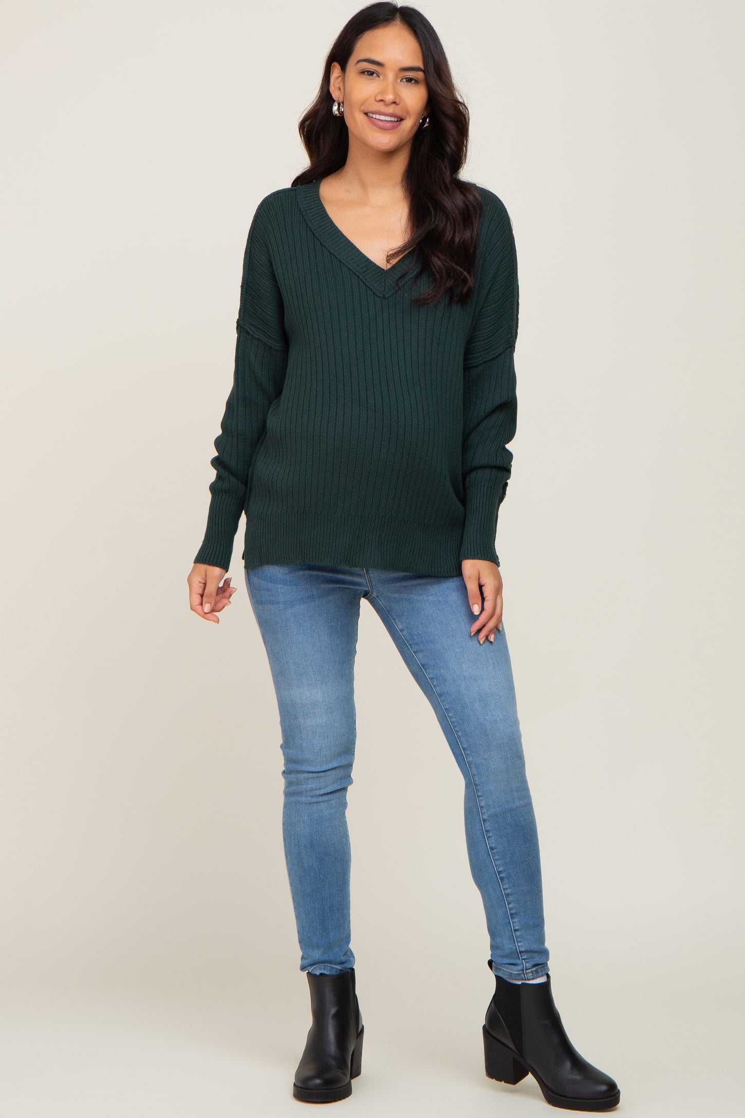 woman wearing a dark green v-neck ribbed maternity sweater with blue skinny jeans and black boots