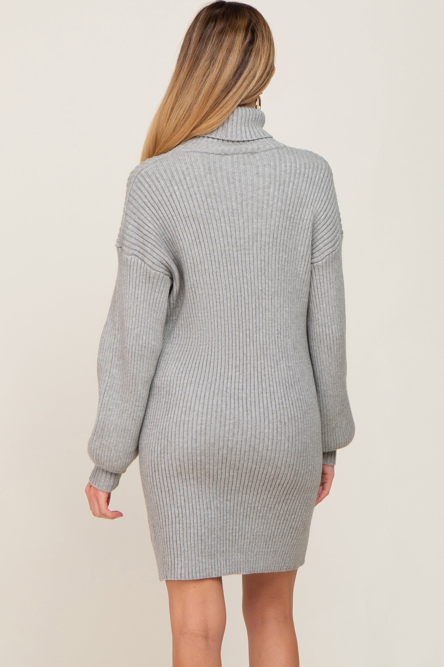 woman wearing a gray ribbed turtleneck sweater dress, showing the back view, designed for maternity wear