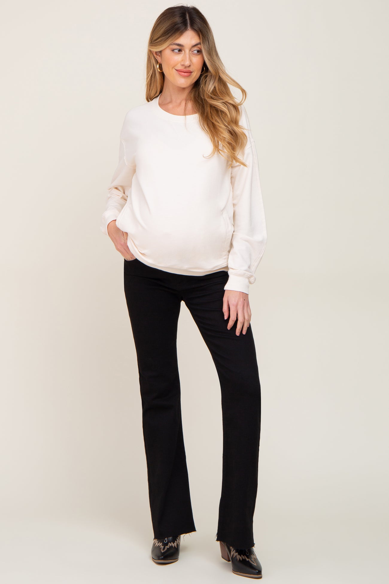 woman wearing a white long sleeve maternity top and black flared maternity pants with a visible baby bump