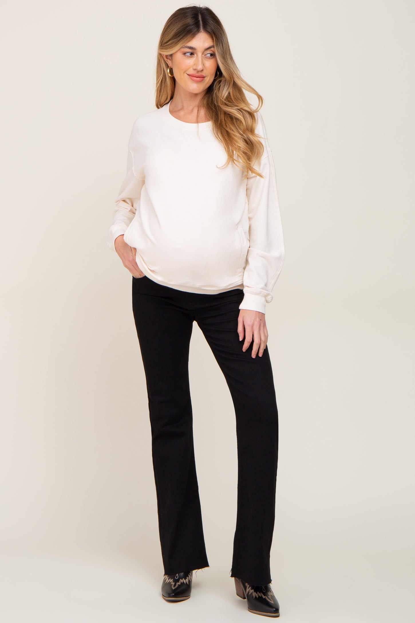 woman wearing a white long sleeve maternity top and black flared maternity pants with a visible baby bump