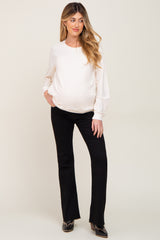 woman wearing a white long sleeve maternity top and black flared maternity pants with a visible baby bump