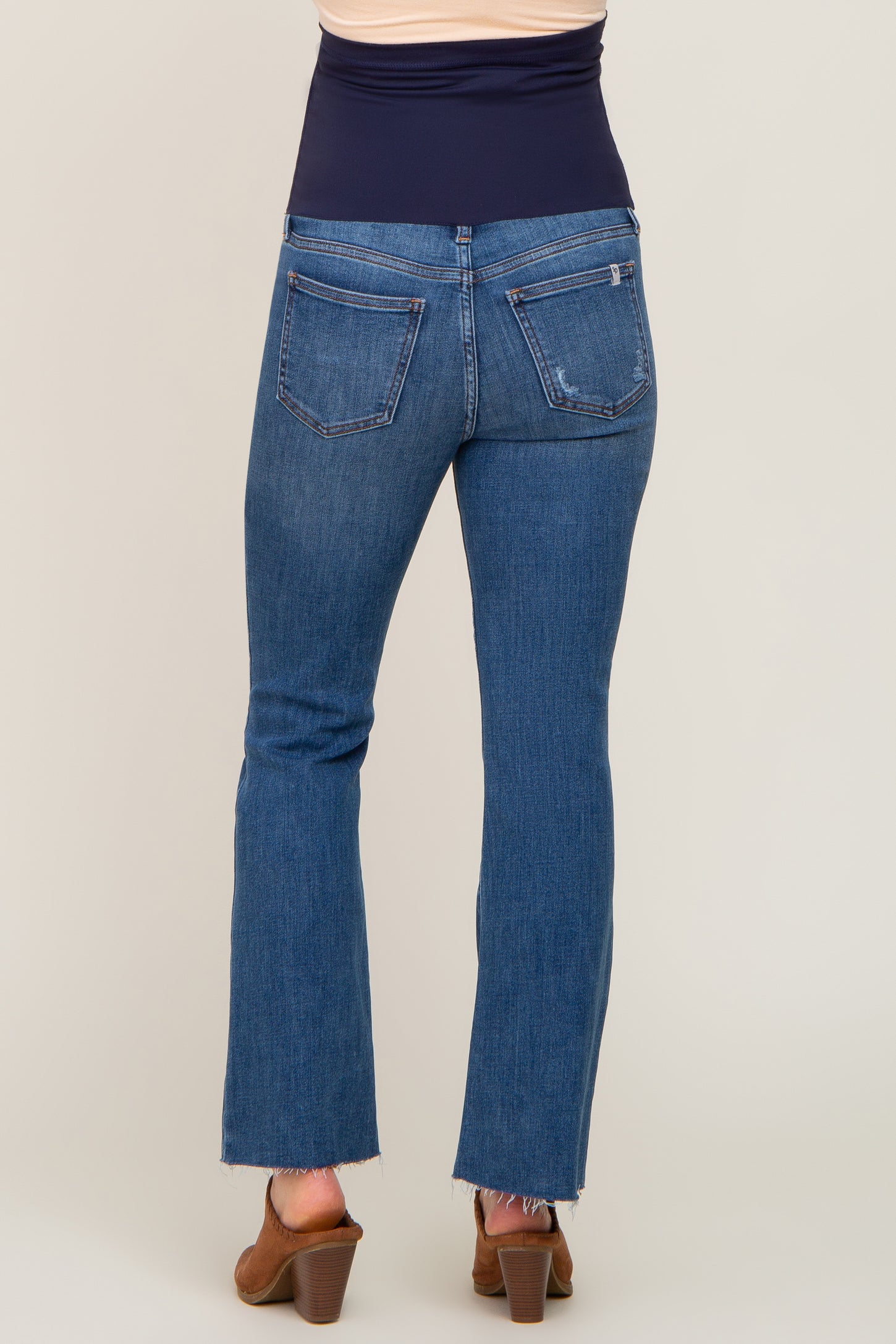 Back view of woman wearing blue maternity flare jeans with a navy belly band and brown heeled mules