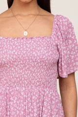 Close up of a woman wearing a purple floral smocked dress with a square neckline and gold pendant necklace