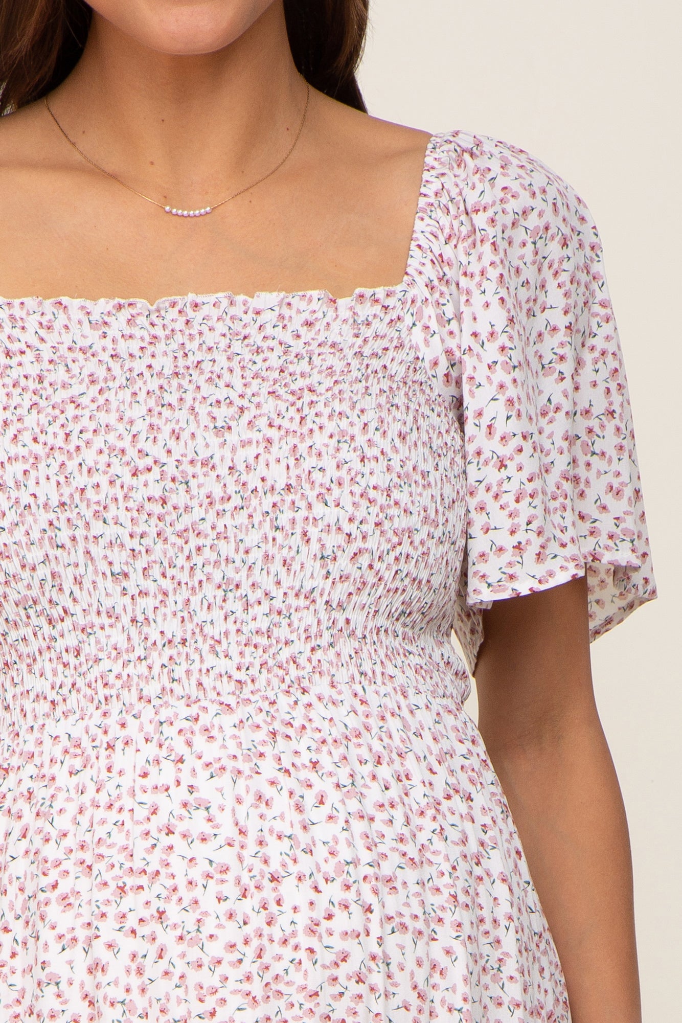 Close up of a woman wearing a white smocked maternity dress with a pink floral print and flutter sleeves