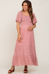woman wearing a pink floral maternity maxi dress with short sleeves and a fitted bodice, cradling her baby bump