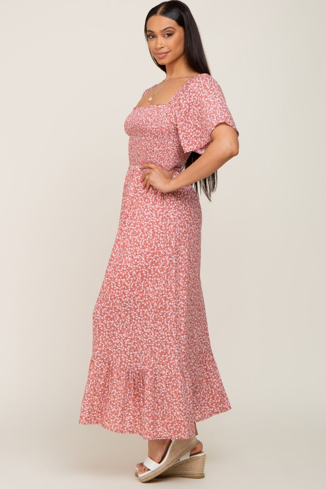 woman wearing a pink floral maxi dress with short sleeves and a smocked bodice, standing sideways on a neutral background