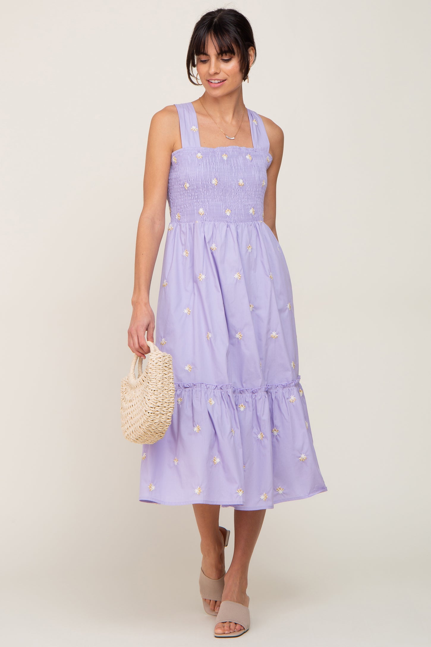 woman wearing lavender smocked midi dress with floral embroidery holding a straw handbag