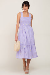 woman wearing lavender smocked midi dress with floral embroidery holding a straw handbag