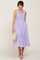 woman wearing lavender smocked midi dress with floral embroidery holding a straw handbag