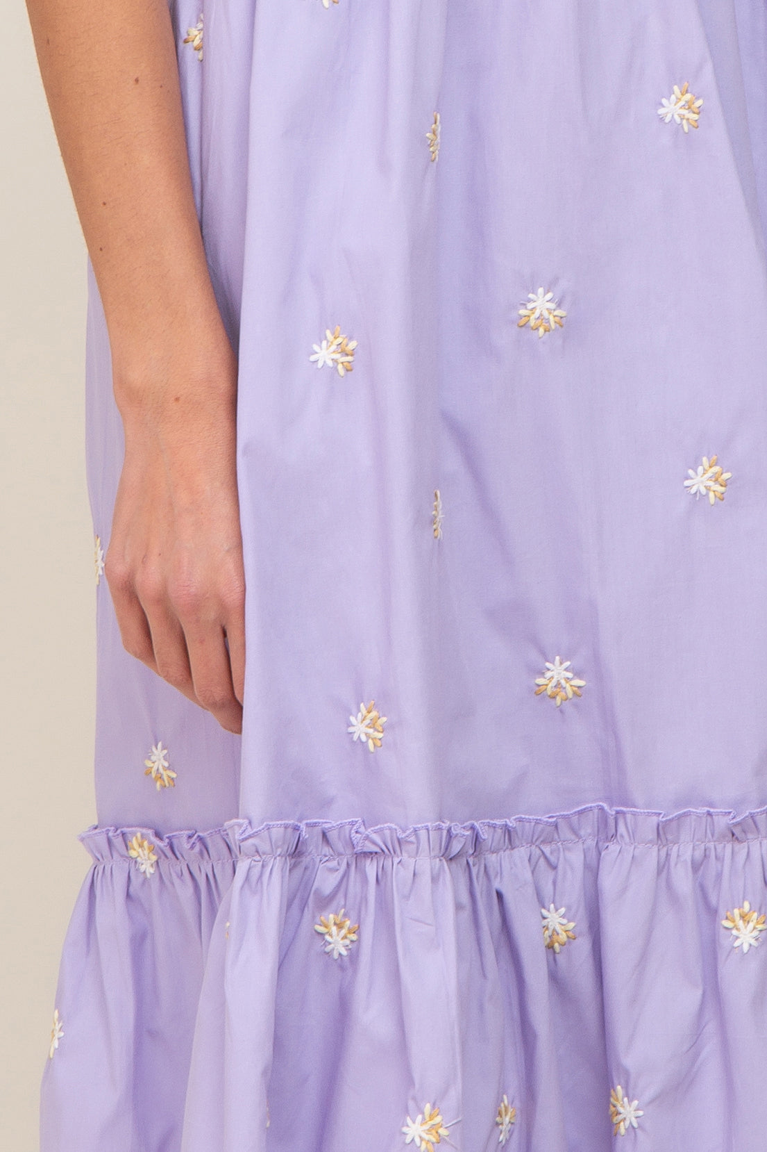 Close up of a lavender dress with white and yellow floral embroidery and a ruffled hemline