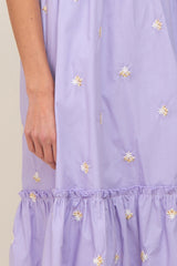 Close up of a lavender dress with white and yellow floral embroidery and a ruffled hemline