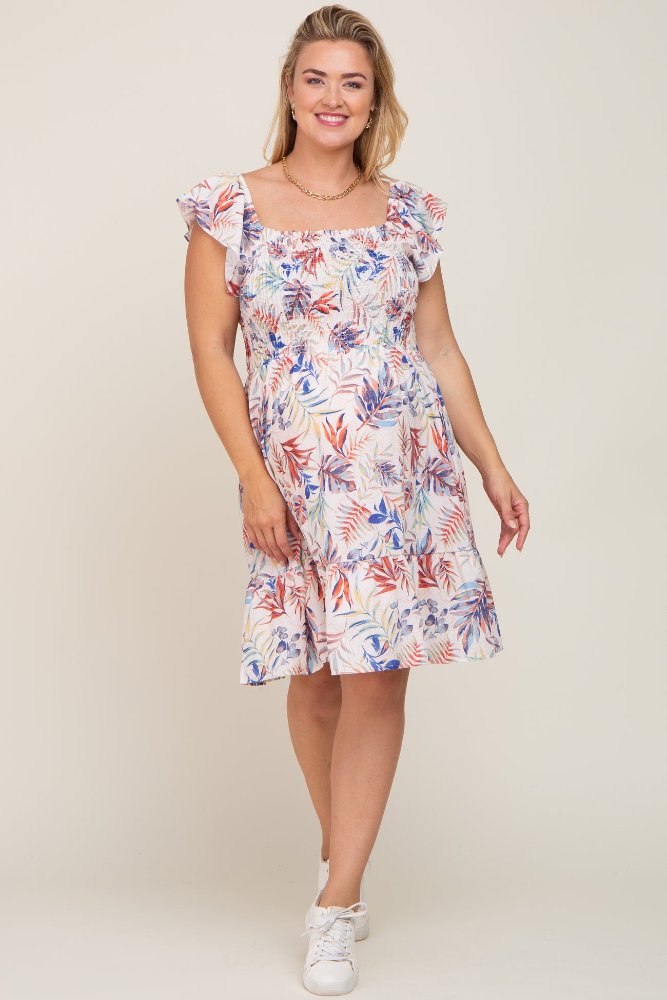 woman wearing a floral smocked maternity dress with ruffle sleeves and white sneakers