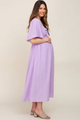 woman wearing a lavender maternity dress with a tie front and flutter sleeves, gently cradling her baby bump