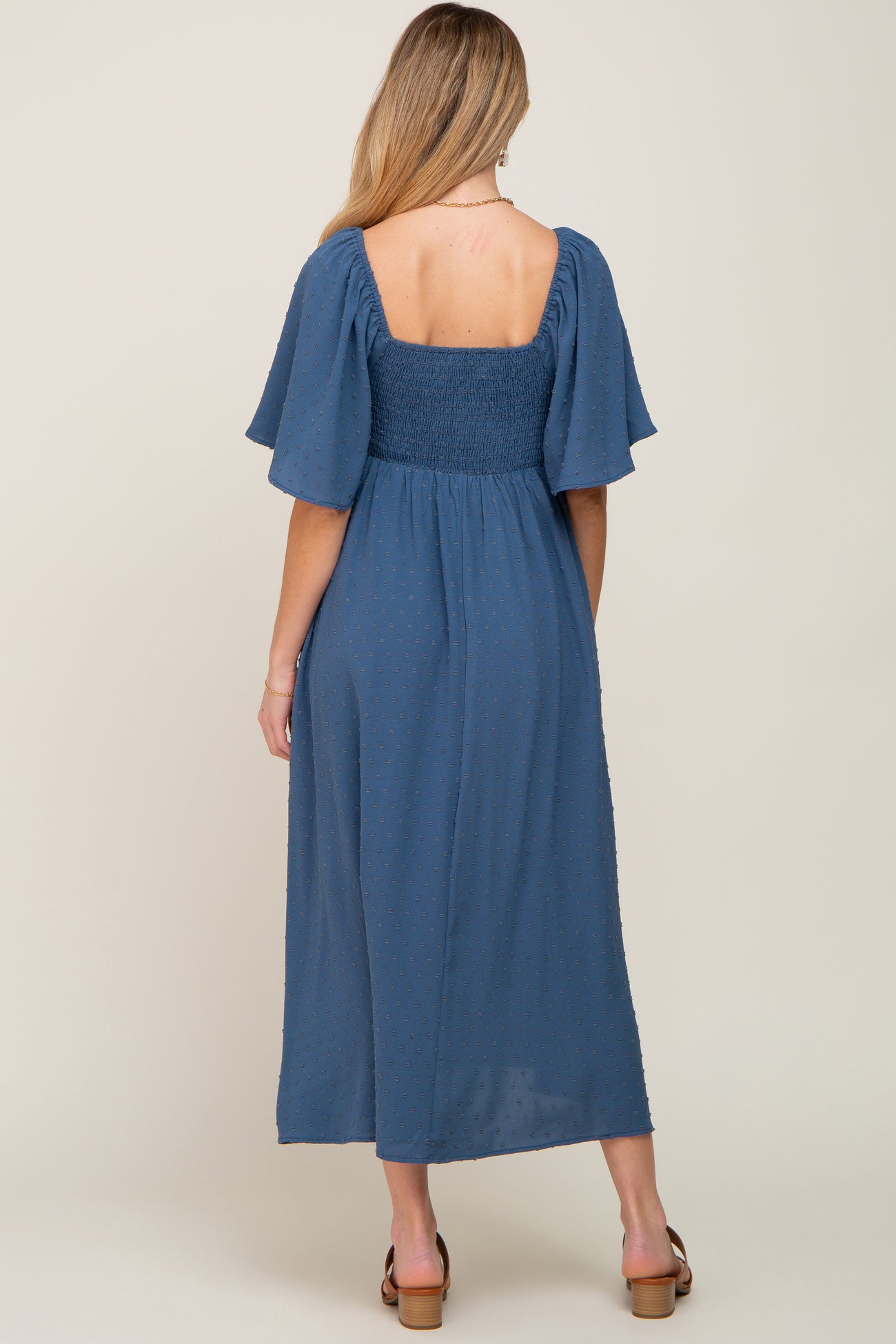 woman wearing a blue maternity maxi dress with short flutter sleeves and a smocked bodice, showing a baby bump