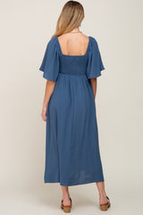 woman wearing a blue maternity maxi dress with short flutter sleeves and a smocked bodice, showing a baby bump