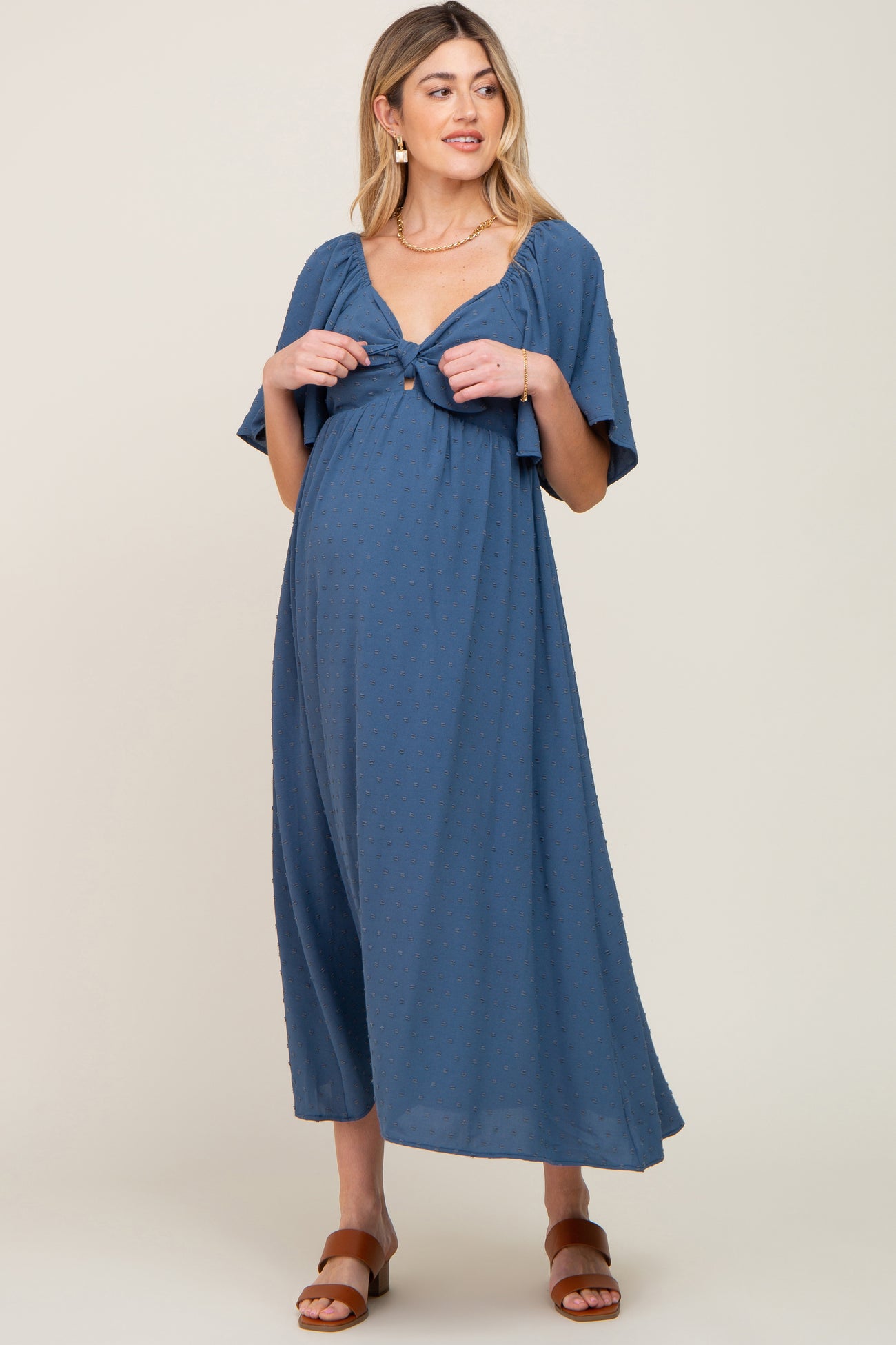 woman wearing a blue maternity maxi dress with a tie detail and short flutter sleeves, showcasing her baby bump