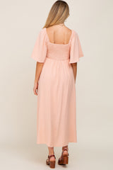 woman wearing a pale pink maternity maxi dress with short flutter sleeves and a smocked waist from the back