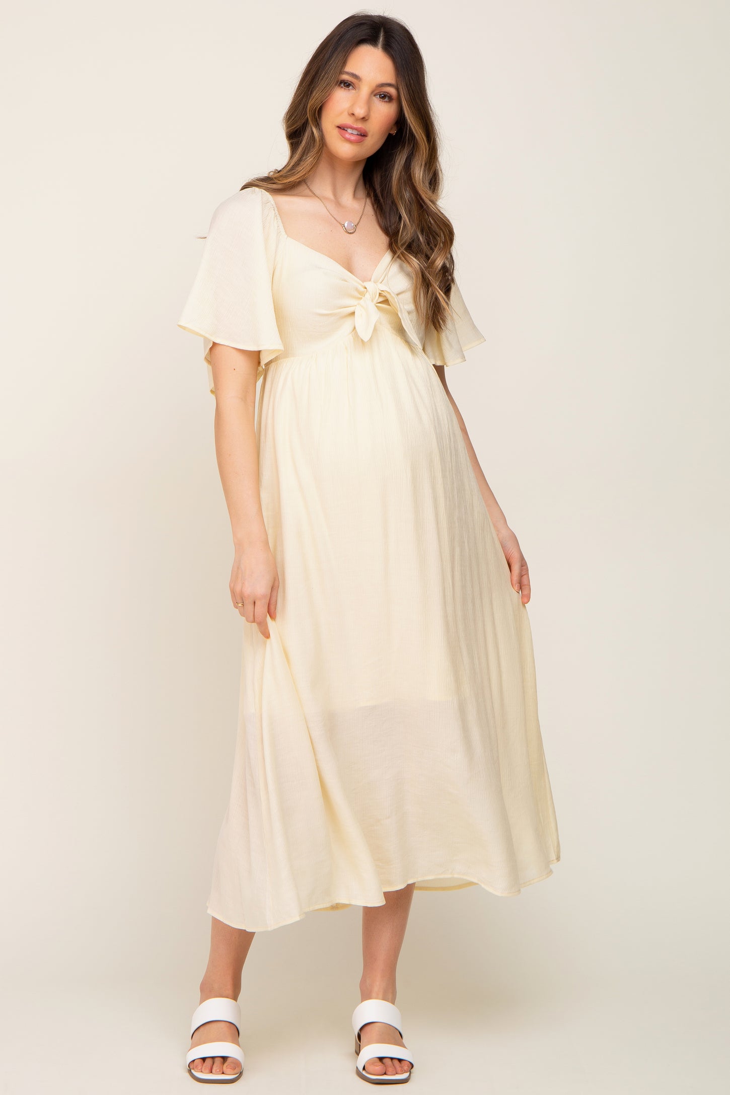 woman wearing a light yellow maternity dress with flutter sleeves and a tie-front detail, showing her baby bump