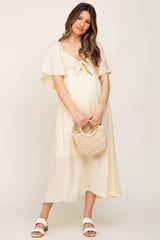 woman wearing a light yellow maternity dress with flutter sleeves and a knot detail, holding a woven handbag and showing her baby bump